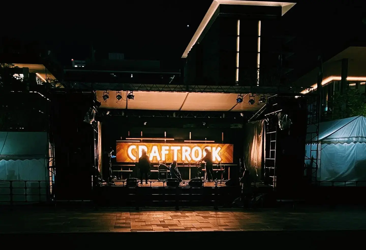 夜の屋外に設置されたCRAFTROCKのライブステージ、オレンジ色の照明に照らされたロゴ看板と演奏するアーティストのシルエット
