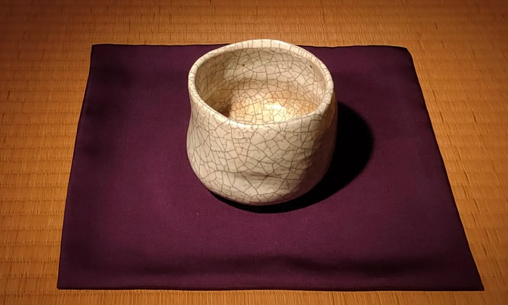 貫入(ひび割れ模様)が美しい和食器の茶碗、紫色の帛紗(ふくさ)の上に置かれている、畳の上の視点