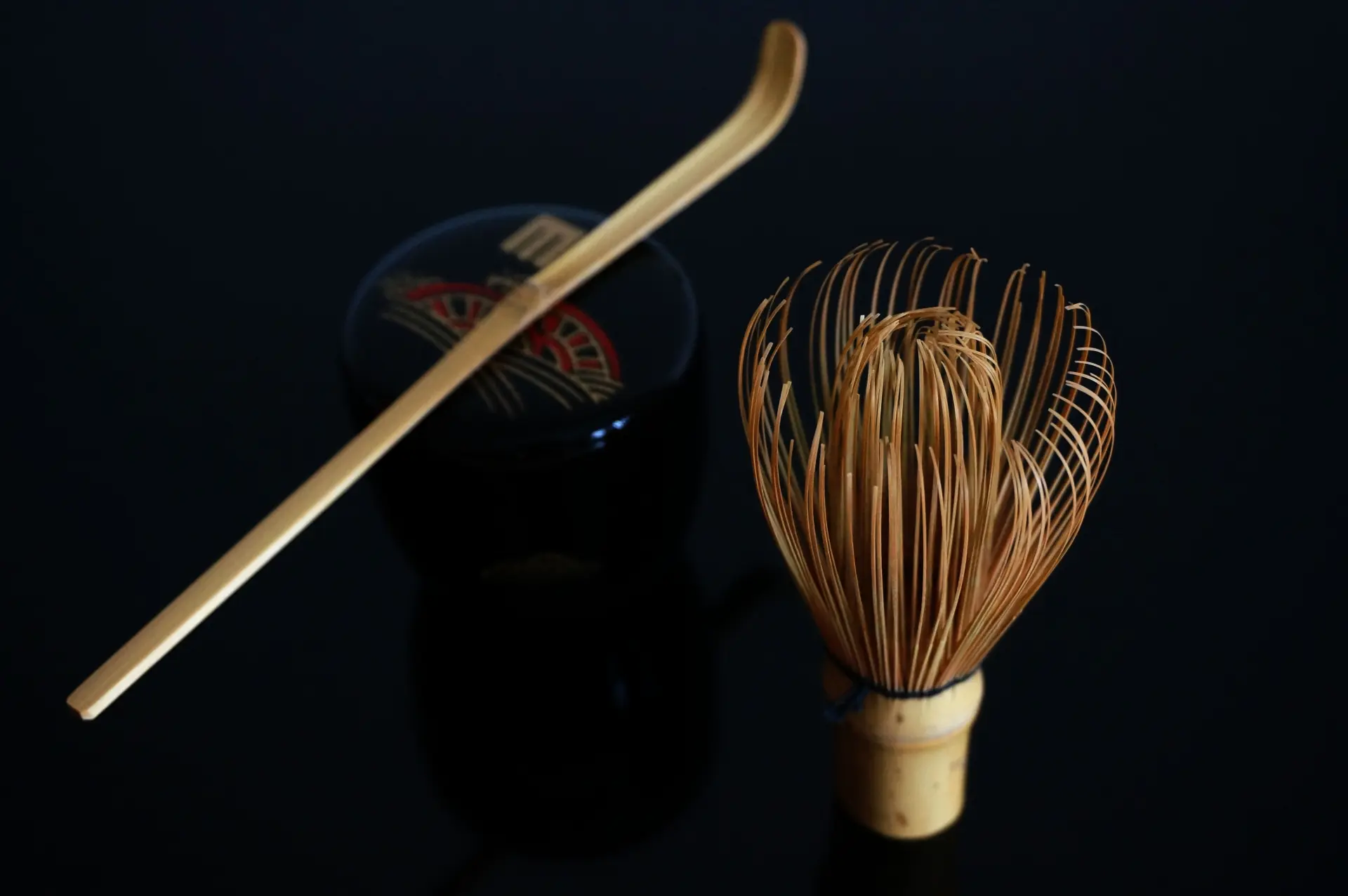 茶道の道具、竹製の茶筅と茶杓、蒔絵が施された黒い茶器(棗)が並んでいる、黒い背景への映り込み