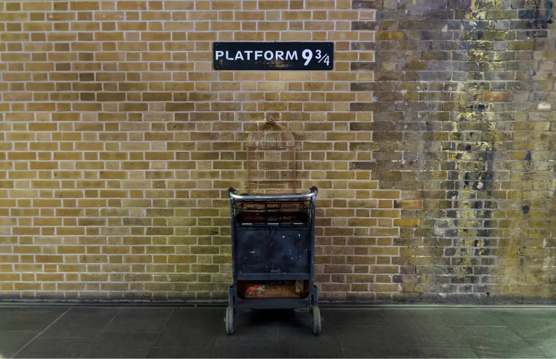 ロンドン、キングス・クロス駅のレンガ壁にある9と3/4番線のプレートと、壁に吸い込まれるように置かれた荷物カート。